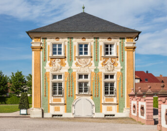 Schloss Bruchsal - Nördliche Orangerie / Nebendienstdienerbau - Von außen / Von Süden - Blick auf die Südfassade der nördlichen Orangerie mit der illusionistischen Fassadenmalerei (ursprünglich gemalt von Giovanni Francesco Marchini, zwischen 1732 und 1737, restauriert von Josef Mariano Kitschker, zwischen 1900 und 1910, erneut restauriert von Klaus Siller (Fassadenmalerei) und  Walter Maschke (Allegorien), 1976) (aufgenommen im April 2018, am späten Nachmittag)