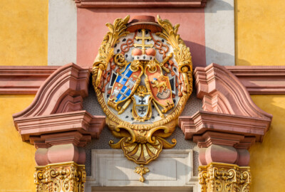Schloss Bruchsal - Hofkirche - Von Norden / Hofseite - Mittelrisalit - Nordportal - Giebel mit Prunkwappen von Kardinal Graf Damian Hugo von Schönborn - Wappenschild links: je zwei Felder für das Hochstift Speyer und die Propstei Weißenburg, Wappenschild unten: Deutschordens-Würden (Landkomtur des Deutschen Ordens in Alden-Biesen (oben) und  Marburg (unten)), Wappenschild rechts: Familien- / Stammwappen von Schönborn (aufgenommen im Mai 2018, am Vormittag)