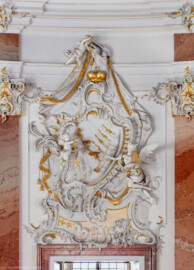 Schloss Bruchsal - Hauptbau - Beletage - Kuppelsaal - Stuckdraperie, oberhalb des Durchgangs zum Marmorsaal - Engel halten Kreuz und Posaune (ursprünglich geschaffen von Johann Michael Feichtmayr) (aufgenommen im Mai 2018, am späten Nachmittag)