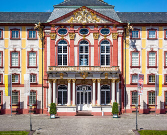 Schloss Bruchsal - Hauptbau - Von Außen / Von Osten / Hofseite - Blick vom Ehrenhof auf die Ostfassade mit dem Mittelrisalit, dem Balkon, dem Fürstensaal und dem Dreiecksgiebel  (aufgenommen im Mai 2018, um die Mittagszeit)