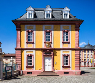 Schloss Bruchsal - Kirchenflügel - Von Osten / Hofseite - Östliche Kopfseite des Kirchenflügels (mit dem Portal zu den ehemaligen Verwaltungsräumen und dem darüber liegenden Prunkwappen von Kardinal Graf Damian Hugo von Schönborn) (aufgenommen im Mai 2018, am frühen Nachmittag)