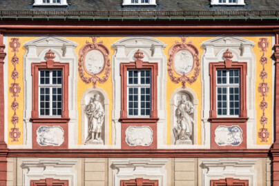 Schloss Bruchsal - Kirchenflügel / Hofkirche / St. Damian und Hugo - Von Westen - Blick vom Kavaliersbau auf die Westfassade der Hofkirche mit den Heiligenfiguren von St. Damian und St. Hugo (gemalt von Walter Maschke), fünf Landschaftgrisaillen und der illusionistischen Fassadenmalerei (ursprünglich gemalt von Giovanni Francesco Marchini, zwischen 1732 und 1737) (aufgenommen im Juli 2018, am frühen Abend)