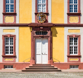 Schloss Bruchsal - Kammerflügel - Von Osten / Hofseite - Ausschnitt aus der östlichen Kopfseite des Kammerflügels (mit dem Portal und dem darüber liegenden Prunkwappen von Kardinal Graf Damian Hugo von Schönborn) (aufgenommen im Juli 2018, am frühen Nachmittag)