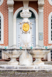 Schloss Bruchsal - Amalienbrunnen / Kanzleibau - Von Westen - Blick vom Vorplatz des Kanzleibaus auf den Amalienbrunnen, auch „Schneckenbrunnen” genannt (entworfen von Fritz Hirsch, aufgestellt 1912; Medaillon entworfen von Heinrich Ehehalt) (aufgenommen im Juli 2018, am späten Nachmittag)
