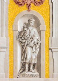 Schloss Bruchsal - Kirchenflügel / Hofkirche / St. Damian und Hugo - Von Westen - Blick vom Kavaliersbau auf die Westfassade der Hofkirche mit der Heiligenfigur von St. Damian (gemalt von Walter Maschke) und der illusionistischen Fassadenmalerei (ursprünglich gemalt von Giovanni Francesco Marchini, zwischen 1732 und 1737) (aufgenommen im August 2018, am späten Nachmittag)
