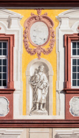 Schloss Bruchsal - Kirchenflügel / Hofkirche / St. Damian und Hugo - Von Westen - Blick vom Kavaliersbau auf die Westfassade der Hofkirche mit der Heiligenfigur von St. Damian (gemalt von Walter Maschke) und der illusionistischen Fassadenmalerei (ursprünglich gemalt von Giovanni Francesco Marchini, zwischen 1732 und 1737) (aufgenommen im September 2018, am späten Nachmittag)