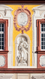 Schloss Bruchsal - Kirchenflügel / Hofkirche / St. Damian und Hugo - Von Westen - Blick vom Kavaliersbau auf die Westfassade der Hofkirche mit der Heiligenfigur von St. Hugo (gemalt von Walter Maschke) und der illusionistischen Fassadenmalerei (ursprünglich gemalt von Giovanni Francesco Marchini, zwischen 1732 und 1737) (aufgenommen im September 2018, am späten Nachmittag)
