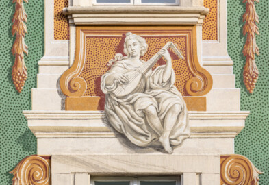Schloss Bruchsal - Südliche Orangerie / Kavaliersbau - Von Außen - Von Westen - Blick auf die 3. (von Norden/von links gezählt) Allegorie bzw. Figur: vermutlich die "Musik" (ursprünglich gemalt von Giovanni Francesco Marchini, zwischen 1732 und 1737, restauriert von Josef Mariano Kitschker, zwischen 1900 und 1910, erneut restauriert von Klaus Siller (Fassadenmalerei) und  Walter Maschke (Allegorien), 1976) (aufgenommen im September 2018, am späten Nachmittag)
