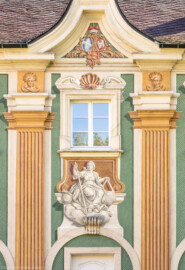 Schloss Bruchsal - Südliche Orangerie / Kavaliersbau - Von Außen - Von Westen - Blick auf die mittlere / 8. (von Norden/von links gezählt) Allegorie bzw. Figur (vermutlich die "Architektur") sowie auf das Allianzwappen im zentralen Giebelfeld / Frontispiz (unten: Wappen des Fürstbischofs Franz Christoph von Hutten zum Stolzenberg, links: Wappen des Hochstifts Speyer, rechts: Wappen der Propstei Weißenburg) (ursprünglich gemalt von Giovanni Francesco Marchini, zwischen 1732 und 1737, restauriert von Josef Mariano Kitschker, zwischen 1900 und 1910, erneut restauriert von Klaus Siller (Fassadenmalerei) und  Walter Maschke (Allegorien), 1976) (aufgenommen im Oktober 2018, am frühen Nachmittag)