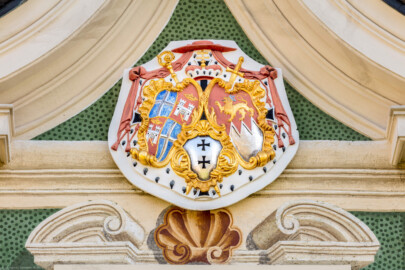 Schloss Bruchsal - Nördliche Orangerie / Nebendienstdienerbau - Von Außen / Von Westen - Gusseisernes Wappenschild im zentralen Giebelfeld - Landeswappen des Fürstbistums Speyer zur Regierungszeit des Fürstbischofs Kardinal Graf Damian Hugo von Schönborn - Links oben und links unten, rechte Hälfte: Wappen des Bistums Speyer, links unten, linke Hälfte: Wappen der Fürstpropstei Weissenburg, rechts: persönliches Wappen von Damian Hugo von Schönborn, Mitte/unten: zweifaches Deutsch-Ordenskreuz für die Ordensballeien Altenbiesen und Hessen (aufgenommen im Oktober 2018, am frühen Nachmittag)
