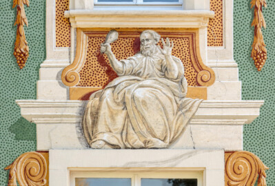 Schloss Bruchsal - Nördliche Orangerie / Nebendienstdienerbau - Von Außen / Von Westen - Blick auf die 13. Allegorie/Figur von Norden/von links; vermutlich Darstellung eines der drei Menschenalter: Greisenalter (ursprünglich gemalt von Giovanni Francesco Marchini, zwischen 1732 und 1737, restauriert von Josef Mariano Kitschker, zwischen 1900 und 1910, erneut restauriert von Klaus Siller (Fassadenmalerei) und  Walter Maschke (Allegorien), 1976) (aufgenommen im Oktober 2018, am Nachmittag)