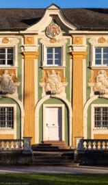 Schloss Bruchsal - Nördliche Orangerie / Nebendienstdienerbau - Von Außen / Von Westen - Blick von der Schlossterrasse auf die Mitte der Westfassade der Orangerie (ursprünglich gemalt von Giovanni Francesco Marchini, zwischen 1732 und 1737, restauriert von Josef Mariano Kitschker, zwischen 1900 und 1910, erneut restauriert von Klaus Siller (Fassadenmalerei) und  Walter Maschke (Allegorien), 1976) (aufgenommen im Oktober 2018, am späten Nachmittag)