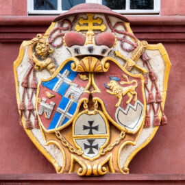 Schloss Bruchsal - Kammerflügel / Amtsgericht - Von Osten / Hofseite - Prunkwappen von Kardinal Graf Damian Hugo von Schönborn über dem Ostportal - Wappenschild links: je zwei Felder für das Hochstift Speyer und die Propstei Weißenburg, Wappenschild unten: Deutschordens-Würden (Landkomtur des Deutschen Ordens in Alden-Biesen (oben) und  Marburg (unten)), Wappenschild rechts: Familien- / Stammwappen von Schönborn (aufgenommen im Oktober 2018, am frühen Nachmittag)