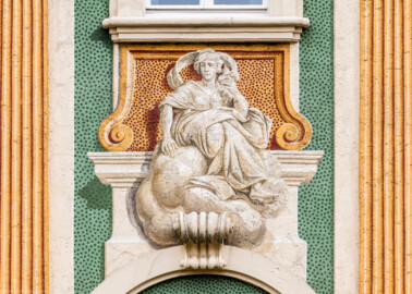 Schloss Bruchsal - Nördliche Orangerie / Nebendienstdienerbau - Von Außen / Von Westen - Blick auf die 9. Allegorie/Figur von Norden/von links; vermutlich Darstellung einer der drei göttlichen Tugenden bzw. theologischen Tugenden: Liebe (ursprünglich gemalt von Giovanni Francesco Marchini, zwischen 1732 und 1737, restauriert von Josef Mariano Kitschker, zwischen 1900 und 1910, erneut restauriert von Klaus Siller (Fassadenmalerei) und  Walter Maschke (Allegorien), 1976) (aufgenommen im Oktober 2018, am Nachmittag)