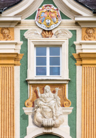 Schloss Bruchsal - Nördliche Orangerie / Nebendienstdienerbau - Von Außen / Von Westen - Blick auf die Mitte der Westfassade mit der Illusionsmalerei und dem Wappenschild (ursprünglich gemalt von Giovanni Francesco Marchini, zwischen 1732 und 1737, restauriert von Josef Mariano Kitschker, zwischen 1900 und 1910, erneut restauriert von Klaus Siller (Fassadenmalerei) und  Walter Maschke (Allegorien), 1976) (aufgenommen im Oktober 2018, am Nachmittag)
