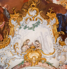 Schloss Bruchsal - Hauptbau / Corps de Logis - Beletage - Marmorsaal / Kaisersaal - Südostecke, oben - Blick auf zwei Putti (als allegorische Darstellung des Winters) sowie umgebende Rokoko-Stuckaturen (Stuckaturen ursprünglich von Johann Michael Feichtmayr) (aufgenommen im Mai 2019, am Nachmittag)