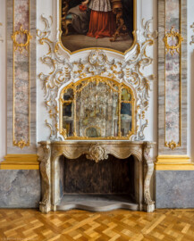 Schloss Bruchsal - Hauptbau / Corps de Logis - Beletage - Fürstensaal - Nordseite, Mitte - Blick auf die Mitte der Nordwand mit den Pilastern, dem Kamin, dem Spiegel, dem reichen Rocaille-Schmuck und dem unteren Teil des Portraits von Damian Hugo Philipp von Schönborn-Buchheim (aufgenommen im Juli 2019, am späten Vormittag)