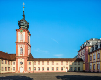 Schloss Bruchsal - Kirchturm / Finsterer Gang / Verbindungsgang - Von Außen / Von Osten - Blick vom ehemaligen südlichen Marstall (heute Parkplatz) auf den Kirchturm der Hofkirche und die Ostseite des Finsteren Gangs, links der Seminarbau / die Pagerie, rechts der Kirchenflügel / die Hofkirche (aufgenommen im August 2019, am Vormittag)