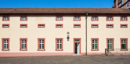 Schloss Bruchsal - Finsterer Gang / Verbindungsgang - Von Außen / Von Osten - Blick vom ehemaligen südlichen Marstall (heute Parkplatz) auf die Ostseite des Finsteren Gangs, rechts der Kirchenflügel (aufgenommen im August 2019, am späten Vormittag)