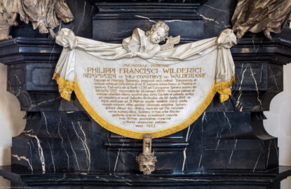Bruchsal - Peterskirche / St. Peter - Östlicher Chorraum -  Von Innen / Von Nordwest - Blick auf das 1923 nachträglich angebrachte Antependium mit einer Inschrift für Philipp Franz Wilderich Nepomuk von Walderdorf am Grabdenkmal für Christoph Franz von Hutten; die Inschrift lautet auf Deutsch: "Dem ewigen Andenken an Philipp Franz Wildreich Nepomuk, aus dem Geschlecht der Grafen des Heiligen Römischen Reiches von Walderdorf, des Bischofs und Fürsten von Speyer, des Propstes der Kirchen des Bistums Trier und der Stiftskirchen St. Paulinus und St. Simon ebendort, des Herrn in Molsberg und Isenburg. Er war geboren am 2. März 1739, auf den Bischofssitz von Speyer erhoben am 22. April 1797, geweiht am 19. Januar 1800. Im großen Unglück (in der Zeit des großen Unglücks) des Vaterlandes und der Kirche ragte seine Tugend umso strahlender durch seine Nächstenliebe (Barmherzigkeit) und seine Herrschaft hervor, viele hat er getröstet und aufgerichtet. Er starb in Bruchsal am 21. April 1810, in der Krypta dieser Kirche St. Peter liegt er bestattet. Deren Tor, das nach Aufnahme des Leichnams des letzten vom ruhreichen alten Stamme (aus der ruhmreichen alten Reihe) der Speyrer Bischöfe verschlossen worden war, wurde in diesen Tagen (wieder) geöffnet. In frommen Gedenken an die von den Bischöfen in dieser Stadt erfolgreich vollbrachten Taten, deren Ruhm die Jahrhunderte verkünden ließen die Bewahrer der Erinnerung an die Heimat diese Grabinschrift im Jahre 1923 setzen." (Epitaph gefertigt von Stephan Strahl und seinem Sohn Johann Strahl) (aufgenommen im August 2019, am Nachmittag)