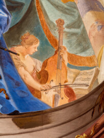 Schloss Bruchsal - Hauptbau / Corps de Logis - Beletage - Fürstensaal - Decke, äußere Zone, westlich, rechts der Mitte - Ausschnitt aus der westlichen äußeren Zone - Ausschnitt aus der Darstellung der sieben Wissenschaften und Künste - Mitte (Frau mit Cello): Darstellung der Musik (Deckenfresko urspünglich gemalt 1751 von Johannes Zick, originalgetreu rekonstruiert 1966 bis 1969 von Wolfram Köberl) (aufgenommen im September 2019, am späten Vormittag) Schloss Bruchsal - Hauptbau / Corps de Logis - Beletage - Fürstensaal - Decke, äußere Zone, westlich, rechts der Mitte - Ausschnitt aus der westlichen äußeren Zone - Ausschnitt aus der Darstellung der sieben Wissenschaften und Künste - Mitte (Frau mit Cello): Darstellung der Musik (Deckenfresko urspünglich gemalt 1751 von Johannes Zick, originalgetreu rekonstruiert 1966 bis 1969 von Wolfram Köberl) (aufgenommen im September 2019, am späten Vormittag)