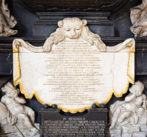 Bruchsal - Peterskirche / St. Peter - Westlicher Chorraum - Doppelgrabdenkmal für Damian Hugo Philipp von Schönborn-Buchheim und für August von Limburg-Stirum - Von Innen / Von Nordost - Blick auf die Gedenktafel für Damian Hugo Philipp von Schönborn-Buchheim mit der Fortsetzung der Tumba-Inschrift am unteren Teil des Grabdenkmals; die Inschrift lautet auf Deutsch: "In das hervorragende Kardinalskollegium der heiligen römischen Kirche aufgenommen am 3. Tag vo dem 1. Dezember (= 29. November) 1713; zur roten Mütze (= Kardinalshut) kamen zwei Bischofshüte: der der Kirche von Speyer im Jahre 1719, am Tag vor dem 1. Dezember (=30. November), der der Kirche von Konstanz am Untersee (0Bodensee) am 4. Tag vor dem 1den des Juli (0 am 12. Juli) im Jahre 1740. Als Fürst beider Staaten erwarb er sich große Verdienste unter den Kaisern Leopold I. , Joseph I. und Karl VI. und war von diesen hochgeschürzt, weil er die ihm von ihnen für das Wohl des Reiches übertragenen Gesandtschaften nach ihrem Wunsch durchgeführt hat. Nach Rom zu den Wahlen der heiligen Päpste reiste er zum wiederholten Male und nahm mit seinen Vorschlägen und Fürsprachen an Ihnen teil. Er stellte die Ordnung der Geistlichkeit, die ungewöhnlich nachlässig war durch äußerst nützliche pastorale Erlasse wieder her, er selbst – zum Vorbild geworden – gründete nach Prüfung des Kirchenvolkes für die Bildung guter Hirten ein Priesterseminar, für Erziehung der Jugend öffentliche Schulen für humanistische Wissenschaften, zum Trost für die Kranken zwei Krankenhäuser und Altenheime, zur Förderung der Frömmigkeit der Gläubigen errichtete er mehr als 10 Kirchen. Für den Deutschen (Ritter-) Orden gründete er auf eigene Kosten eine neue Präfektur, für die Wiederreichtung des Speyrer Doms aus den Trümmern vermachte er testamentarisch viele tausend (Gold-) Münzen. Sein Herrschaftsgebiet, das er verschuldet vorgefunden hatte, beschenkte er mit überreichen Einkünften und sehr großen Schätzen, ohne eine andere als die alte maßvolle Steuer einzufordern; sparsam immer im eigenen Hause, in der Ausstattung öffentlicher Gebäude und im Bau der landesherrlichen Straßen großartig, wurde er, um die Belohnung für seine geistlichen Sorgen zu empfangen, in den Himmel gerufen und starb am 14. Tag vor dem 1. September (= am 19. August) im Jahre 1743." (Epitaph entworfen von Johann Seitz, gefertigt von Stephan Strahl, Figuren gefertigt von Ferdindanz Diez, vorgelagerter Marmoraltar und dazugehörende Plastiken gefertigt von Joachim Günther) (aufgenommen im September 2019, um die Mittagszeit)