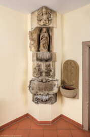 Waghäusel - Kloster - Von innen - Raum östlich der Sakristei - Von Nordost - Blick auf die originalen Sandsteinarbeiten: Madonna, Wappen der Gründer und Gedenktafel zur Erbauung des Klosters 1640 (Inschrift: „ANO 1640 / P. NOBILIS STRENUUS AC GRATIOSUS DNS D / CASPARIUS BAUMBERGER A RAUENBERG DNS IN LOR / (B)ISWEILER HANHAVEN COLONELLUS ET COMEND / PHILIPSBURGENSIS ET P NOBILIS DANN ANNA / HONDT A SAULHEIM HUNC PP CAPUCINOR` CONVEN / TUM SUIS SUMPTIBUS EXSTRUI FECERUNT“ / Übersetzt in etwa: Der hochedle Caspar von Baumberger, vermählt mit der Anna geb. Hund von Saulheim, Oberst und Kommandant zu Philippsburg, Herr von Rauenberg, Herr in Lahr, Bischweiler sowie Hanhofen, ließ im Jahre 1640 das Kapuzinerkonvent Waghäusel, kath. Wallfahrtskirche St. Maria auf seine Kosten erbauen) (hier die Sandsteinarbeiten im Original, heute im Innern des Klosters; eine Kopie findet sich heute außen am nordöstlichen Eckpfeiler des Kapuzinerchors) (aufgenommen im Dezember 2019, am späten Nachmittag)