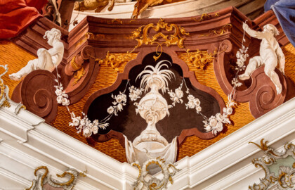 Schloss Bruchsal - Hauptbau / Corps de Logis - Beletage - Fürstensaal - Decke, äußere Zone, Südwestecke - Ausschnitt aus der südwestlichen äußeren Zone - Ausschnitt aus der Darstellung der Jagd, ein wichtiger Wirtschaftszweig Bruchsals - Unten: Scheinarchitektur mit zwei Putti (Deckenfresko urspünglich gemalt 1751 von Johannes Zick, originalgetreu rekonstruiert 1966 bis 1969 von Wolfram Köberl) (aufgenommen im Januar 2020, am späten Vormittag)