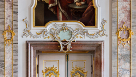 Schloss Bruchsal - Hauptbau / Corps de Logis - Beletage - Fürstensaal - Nordseite, westlich - Blick auf Rocaille-Verzierungen im Bereich der Tür, zwei Pilaster und den unteren Teil des Portraits von Eberhard von Dienheim (aufgenommen im März 2020, am frühen Nachmittag)