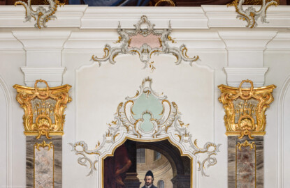Schloss Bruchsal - Hauptbau / Corps de Logis - Beletage - Fürstensaal - Westwand, Mitte, oben - Blick auf reichhaltige Rocaille-Verzierungen, zwei Pilaster mit Kapitellen und dem oberen Teil des Portraits von Eberhard von Dienheim (aufgenommen im März 2020, am frühen Nachmittag)
