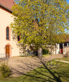 Waghäusel - Wallfahrtskirche - Von Außen / Von Südwesten - Blick auf die Südostseite der Kirche (links), die Gedenktafel für verstorbene Kapuziner von Waghäusel (Mitte) und die Edith-Stein-Halle (rechts) (aufgenommen im April 2020, am späten Nachmittag)