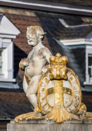 Schloss Bruchsal - Garten - Westeingang / Haltestelle Schlossgarten - Nördlicher Torpfosten - Von Südwesten - Blick auf einen Putto und eine Kartusche mit Bischofshut und Wappen des Hochstifts Speyer (aufgenommen im April 2020, am frühen Abend)