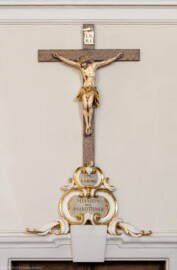 Bruchsal - Peterskirche / St. Peter - Längsschiff / Westwand - Von Osten - Blick auf ein Kruzifix sowie auf eine Gedenkinschrift einer Mission der Pallottiner (der Gesellschaft des katholischen Apostolates) über der Tür zum westlichen Oratorium (aufgenommen im April 2020, am späten Nachmittag)
