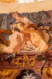 Schloss Bruchsal - Hauptbau / Corps de Logis - Beletage - Fürstensaal - Decke, äußere Zone, Südostecke - Ausschnitt aus der südöstlichen äußeren Zone - Ausschnitt aus der Darstellung des Weinbaus, ein wichtiger Wirtschaftszweig Bruchsals - Mittig oben (Mann/Frau mit Weinlaubkrone und Korb mit Weintrauben): Darstellung des griechischen / römischen Weingottes Dionysos / Bacchus; mittig unten (mannartige Figuren): Darstellung von Satyrn, mit Bocks-Beinen und -Ohren (Deckenfresko urspünglich gemalt 1751 von Johannes Zick, originalgetreu rekonstruiert 1966 bis 1969 von Wolfram Köberl) (aufgenommen im Mai 2020, am späten Vormittag) Schloss Bruchsal - Hauptbau / Corps de Logis - Beletage - Fürstensaal - Decke, äußere Zone, Südostecke - Ausschnitt aus der südöstlichen äußeren Zone - Ausschnitt aus der Darstellung des Weinbaus, ein wichtiger Wirtschaftszweig Bruchsals - Mittig oben (Mann/Frau mit Weinlaubkrone und Korb mit Weintrauben): Darstellung des griechischen / römischen Weingottes Dionysos / Bacchus; mittig unten (mannartige Figuren): Darstellung von Satyrn, mit Bocks-Beinen und -Ohren (Deckenfresko urspünglich gemalt 1751 von Johannes Zick, originalgetreu rekonstruiert 1966 bis 1969 von Wolfram Köberl) (aufgenommen im Mai 2020, am späten Vormittag)