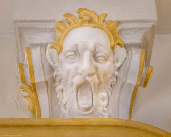 Schloss Bruchsal - Hauptbau / Corps de Logis - Von innen - Nordöstliche Dienertreppe - Erstes Obergeschoss (Zwischengeschoss) - Von Osten - Blick auf die Kopfskulptur am oberen Säulenabschluss der nördlichen Säule (aufgenommen im Oktober 2020, um die Mittagszeit) Schloss Bruchsal - Hauptbau / Corps de Logis - Von innen - Nordöstliche Dienertreppe - Erstes Obergeschoss (Zwischengeschoss) - Von Osten - Blick auf die Kopfskulptur am oberen Säulenabschluss der nördlichen Säule (aufgenommen im Oktober 2020, um die Mittagszeit)