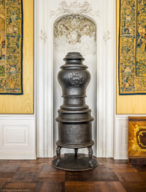 Schloss Bruchsal - Hauptbau / Corps de Logis - Von innen - Beletage - Gelbes Zimmer - Ostwand, Mitte - Blick auf die östliche Ofennische und den Stubenofen aus Gusseisen (sog. Kanonenofen) mit dem fürstbischöflichen Wappen von Franz Christoph von Hutten zum Stolzenberg (hergestellt wohl um 1761; Gewicht ca. 250 kg; beschädigt beim Brand 1945, wohl nach 2000 wiederhergestellt, u.a. durch Restauratorin Magdalena Baur und der Kunstschmiede Peter Klink aus Pfullendorf) (aufgenommen im November 2020, um die Mittagszeit)