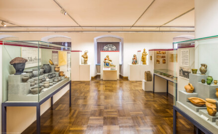 Städtisches Museum Bruchsal - Schloss Bruchsal - Hauptbau / Corps de Logis - Südlicher Raum, Bereich Mittelalter bis Neuzeit - Blick nach Süden, links eine Vitrine mit Keramikfunden aus dem Alten Schloss, eine alte Stadtansicht und ein alter Plan von Bruchsal, in der Mitte die Skulpturen (v.l.n.r.) St. Nepomuk, Pietà (Vesperbild), Hl. Maria, Madonna mit dem Jesuskind, rechts Exponate zum ehemaligen Bruchsaler Kapuzinerkloster sowie Vitrinen mit Keramik- und Glasfunden (aufgenommen im November 2020, am späten Vormittag)