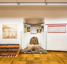 Städtisches Museum Bruchsal - Schloss Bruchsal - Hauptbau / Corps de Logis - Von innen - Südlicher Raum, Bereich Latènezeit - Von Süden - Blick auf einen nachgebauten Rennofen zur experimentellen Eisenverhüttung (Mitte) sowie einen Eisenbarrenfund mit 53 Doppelpyramidenbarren (links) (aufgenommen im November 2020, am frühen Nachmittag)