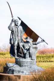 Waghäusel - Eremitage - Von Außen - Von Süden - Blick auf das Freiheitsdenkmal zum Gedenken an die Schlacht bei Waghäusel 1849 (Senkrechte Inschrift: "Den Wegbereitern der Demokratie - 21. Juni 1999"; schräge Inschrift: "In dankbarer Erinnerung an den Einsatz vieler Männer und Frauen für Freiheit und Menschenrechte in der Badischen Revolution von 1848-1849 wurde dieses Denkmal von der Stadt Waghäusel zum 150. Jahrestag der Schlacht von Waghäusel und des Gefechtes von Wiesental errichtet"; Inschrift in der Fahne: "Fond. Veneta d'Arte Verona Italia") (Skulptur aus Bronze, geschaffen 1999 von dem Speyerer Künstler Franz-Werner Müller-Steinfurt (1952-2017)) (aufgenommen im Februar 2021, um die Mittagszeit)