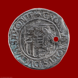 Städtisches Museum Bruchsal - Schloss Bruchsal - Hauptbau / Corps de Logis - Münzsammlung - Revers (Rückseite) der Münze "Silberner Engelsgroschen" (dünn, Durchmesser 28 mm, mit Loch; Avers: Halbfigur eines Engels, Wappenschild mit zwei gekreuzten Schwertern, umlaufender Schriftzug FRIDERICUS JOHANNES GEORGIUS (verweist auf Kurfürst Friedrich III., Herzog Johann der Beständige und Herzog Georg der Bärtige); Revers: großes dreiteiliges Wappenschild (Allianzwappen der drei Herzöge), umlaufender Schriftzug GROSSVS NOVVS DVCVM SAXONIE (neuer Groschen der Herzöge von Sachsen); geprägt 1512 in Annaberg / Sachsen von Albrecht von Schreibersdorf; Fundort/-zeit: Bruchsal, Kaiserstraße, wohl 1948; Informationen recherchiert durch Doris Buhlinger M.A.); (aufgenommen im April 2021, am Nachmittag) Städtisches Museum Bruchsal - Schloss Bruchsal - Hauptbau / Corps de Logis - Münzsammlung - Revers (Rückseite) der Münze "Silberner Engelsgroschen" (dünn, Durchmesser 28 mm, mit Loch; Avers: Halbfigur eines Engels, Wappenschild mit zwei gekreuzten Schwertern, umlaufender Schriftzug FRIDERICUS JOHANNES GEORGIUS (verweist auf Kurfürst Friedrich III., Herzog Johann der Beständige und Herzog Georg der Bärtige); Revers: großes dreiteiliges Wappenschild (Allianzwappen der drei Herzöge), umlaufender Schriftzug GROSSVS NOVVS DVCVM SAXONIE (neuer Groschen der Herzöge von Sachsen); geprägt 1512 in Annaberg / Sachsen von Albrecht von Schreibersdorf; Fundort/-zeit: Bruchsal, Kaiserstraße, wohl 1948; Informationen recherchiert durch Doris Buhlinger M.A.); (aufgenommen im April 2021, am Nachmittag)