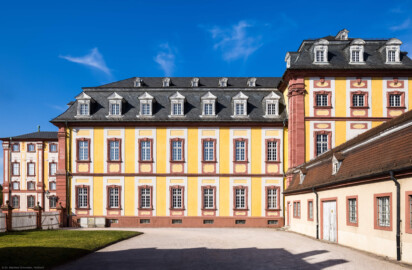 Schloss Bruchsal - Kirchenflügel / Hofkirche - Von Süden - Blick vom heutigen Parkplatz vor der ehemaligen Hofsattlerei (bzw. neben der ehemaligen Hofapotheke) nach Norden auf den südwestlichen Teil und den Mittelrisalit des Kirchenflügels, links der Südwestteil des Hauptbaus, rechts die Westseite der Hofmesnerswohnung bzw. des Finsteren Gangs (Verbindungsgang zwischen Hofkirche und Kirchturm) (aufgenommen im April 2021, am späten Nachmittag)