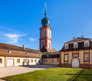 Schloss Bruchsal - Von außen - Kirchturm / Verbindungsgang / Hofmesnerswohnung / Hofsattlerei / Hofapotheke - Von Nordwesten - Blick von der Südwestecke des Kirchenflügels nach Südosten auf den Kirchturm, links die Hofmesnerswohnung bzw. der Finstere Gang (Verbindungsgang zwischen Hofkirche und Kirchturm), in der Mitte die Hofsattlerei, rechts die Hofapotheke (aufgenommen im April 2021, am späten Nachmittag)