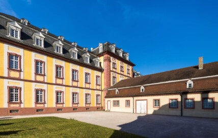 Schloss Bruchsal - Kirchenflügel / Hofkirche / Finsterer Gang - Von Südwesten - Blick von der Nordwestecke der Hofapotheke nach Nordosten auf den südwestlichen Teil und den Mittelrisalit des Kirchenflügels, rechts die Westseite der Hofmesnerswohnung bzw. des Finsteren Gangs (Verbindungsgang zwischen Hofkirche und Kirchturm) (aufgenommen im April 2021, am frühen Abend)