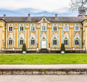Schloss Bruchsal - Südliche Orangerie / Kavaliersbau - Von Außen - Von Westen - Blick auf den Mittelteil der Westfassade der Orangerie (Fassade der Orangerie ursprünglich gemalt von Giovanni Francesco Marchini, zwischen 1732 und 1737, restauriert von Josef Mariano Kitschker, zwischen 1900 und 1910, erneut restauriert von Klaus Siller (Fassadenmalerei) und  Walter Maschke (Allegorien), 1976) (aufgenommen im Mai 2021, am  Nachmittag)