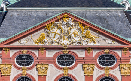 Schloss Bruchsal - Hauptbau - Von Außen - Von Osten / Hofseite - Blick von der Plattform des Kanzleibaus auf den oberen Teil des Mittelrisalits der Ostfassade und auf den Dreiecksgiebel mit dem Wappen (unten: Familienwappen des Kardinals Schönborn, links: Wappen des Hochstift Speyer, rechts: Wappen der Propstei Weißenburg; Inschrift im Giebelfeld, unten rechts "renoviert 1902 1936", unten links "rest. 1954") (aufgenommen im Juni 2021, am Vormittag)