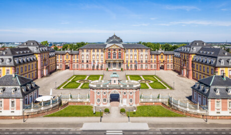 Schloss Bruchsal - Zentrum der Schlossanlage - Von Außen - Von Osten / Von oben - Blick von der Plattform des Kanzleibaus nach unten auf die Dreiflügelanlage; in der Mitte der Hauptbau / das Corps de Logis, links der Mitte der südliche Verbindungsbau, links davon der Kirchenflügel / die Hofkirche / St. Damian und Hugo, rechts der Mitte der nördliche Verbindungsbau, rechts davon der Kammerflügel / das Amtsgericht; vorne links das Hofzahlamt (heute Schlosscafé), vorne in der Mitte das Torwachtgebäude, vorne rechts das Hofkontrollamt; in der Mitte der Anlage der Ehrenhof (aufgenommen im Juni 2021, am späten Vormittag)
