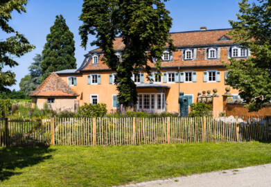 Waghäusel - Eremitage - Von Außen - Von Südost - Blick vom südwestlichen Wegzugang auf den südwestlichen Kavalierspavillon (den "Fremdenbau"), links das Jagdhäuschen, davor der "Hochzeitsgarten" (aufgenommen im Juli 2021, am späten Vormittag)