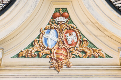 Schloss Bruchsal - Südliche Orangerie / Kavaliersbau - Von Außen - Von Westen - Blick auf das Allianzwappen im zentralen Giebelfeld / Frontispiz (unten: Wappen des Fürstbischofs Franz Christoph von Hutten zum Stolzenberg, links: Wappen des Hochstifts Speyer, rechts: Wappen der Propstei Weißenburg) (ursprünglich gemalt von Giovanni Francesco Marchini, zwischen 1732 und 1737, restauriert von Josef Mariano Kitschker, zwischen 1900 und 1910, erneut restauriert von Klaus Siller (Fassadenmalerei)) (aufgenommen im März 2022, am frühen Nachmittag)