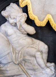 Bruchsal - Peterskirche / St. Peter - Westlicher Chorraum - Doppelgrabdenkmal für Damian Hugo Philipp von Schönborn-Buchheim und für August von Limburg-Stirum - Von Nordost - Blick auf die trauernde Knabenfigur / einen Putto (links unten am Grabdenkmal; gefertigt von Joachim Günther) (aufgenommen im März 2022, am frühen Nachmittag, nach der Renovierung)
