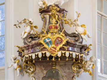 Bruchsal - Peterskirche / St. Peter - Von Innen - Von Südwesten - Kanzel - Blick auf den reichhaltig geschmückten Schalldeckel der Kanzel - In der Mitte das bischöfliche speyerische Hutten-Wappen (links oben: Wappen des Bistums Speyer, rechts oben: Wappen der Fürstpropstei Weissenburg, mitte unten: Familienwappen von Franz Christoph von Hutten zum Stolzenberg) (Kanzel geschaffen von Johann Michael Feuchtmayer, 1756; Altar erstellt 1996) (aufgenommen im März 2022, am Nachmittag, nach der Renovierung)